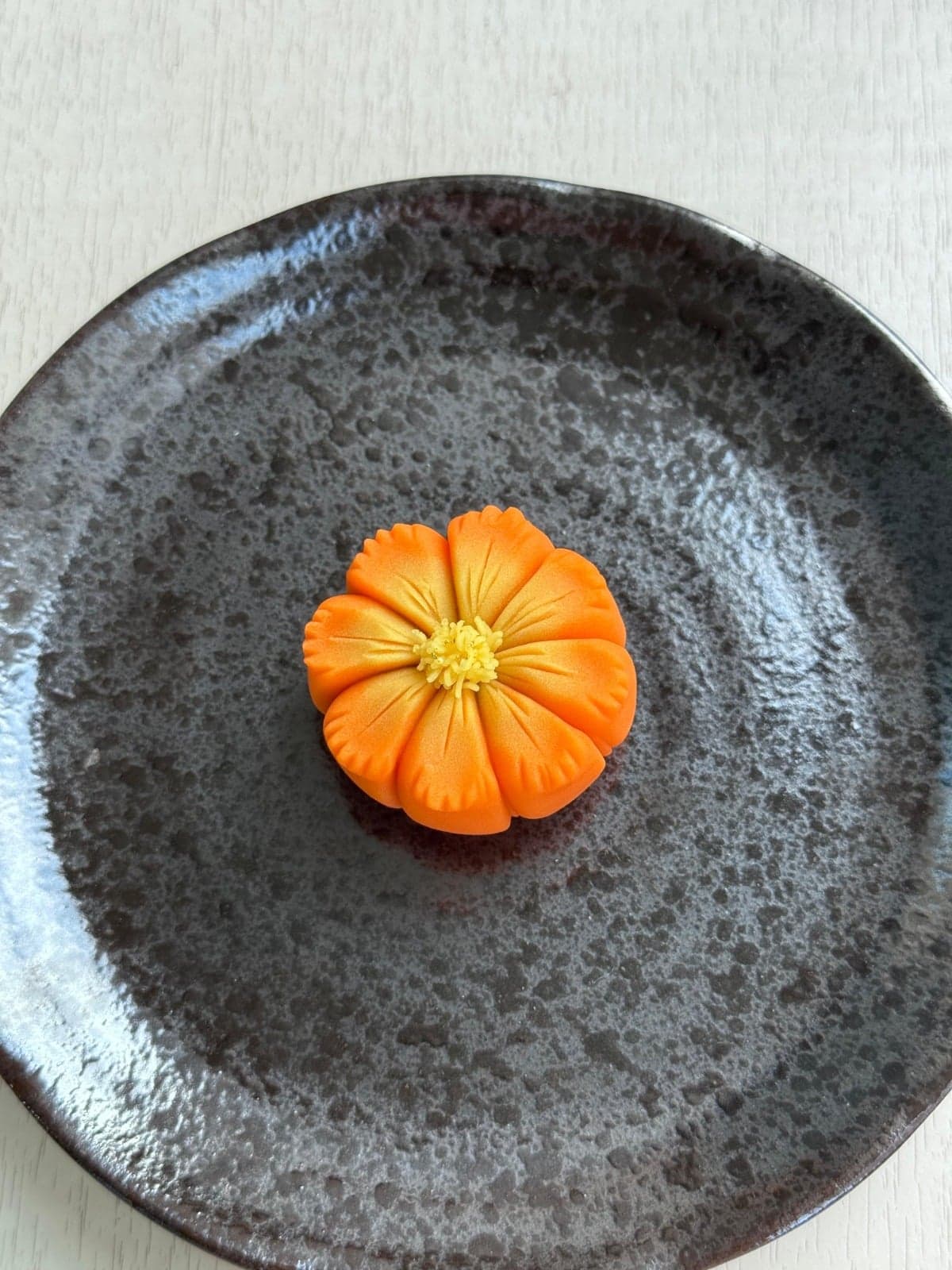 Orange chrysanthemum-shaped nerikiri on a dark speckled plate